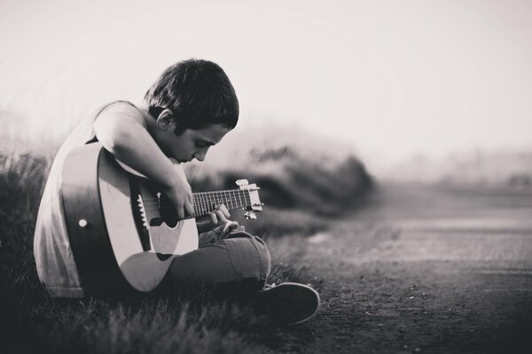 The boy plays a melody on the guitar