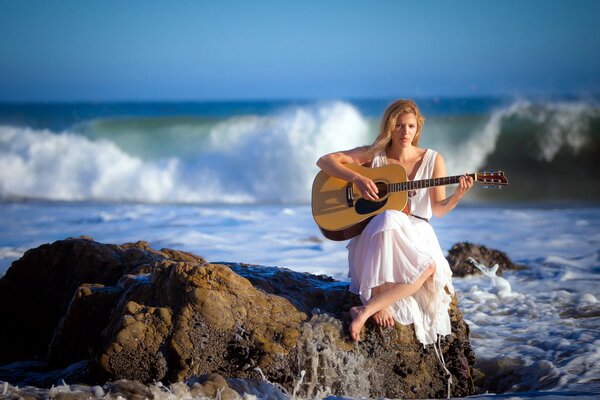 A girl is sitting on the shore of the surf with a guitar