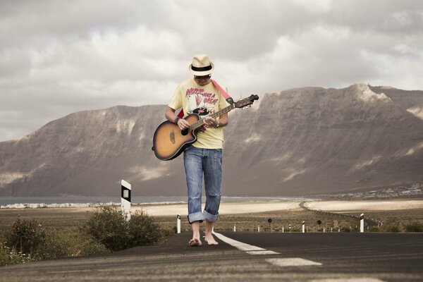 A guy with a guitar is walking down the road
