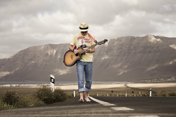 Un gars avec une guitare marche sur la route