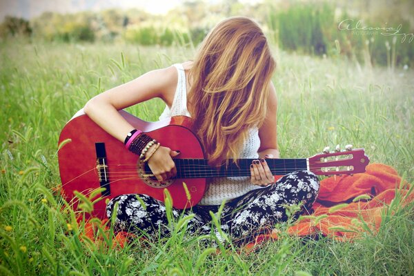 Fille avec une guitare est assis sur l herbe