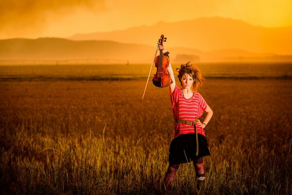 A violinist girl at sunset in a field