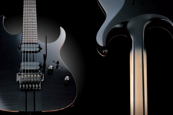 Two black electric guitars on a black background