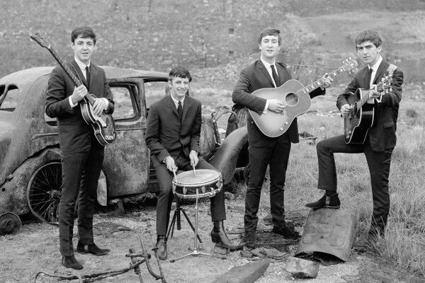 Photo en noir et blanc du groupe des Beatles devant une voiture rouillée