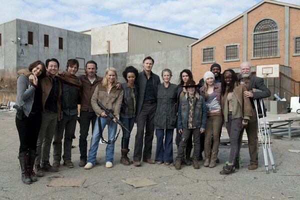 Group photo of the smiling actors of the TV series The Walking Dead against the backdrop of the scenery of houses