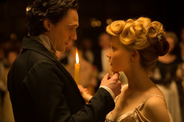 Actors Hiddleston and Mia Wasikowska in a romantic shot against the background of a burning candle and the guests of the ball