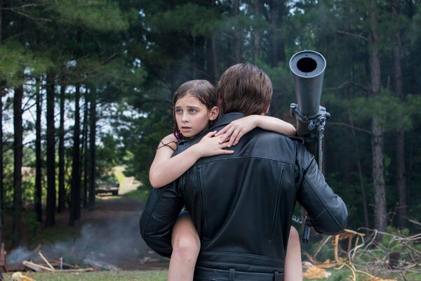 Une image du film Terminator: genisys, où sur le fond de la forêt, un homme porte une fille dans ses bras