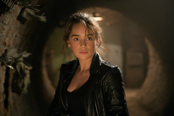A shot from the movie Terminator: genesis, where the heroine of Emilia Clarke stands in a leather jacket against the background of a stone vault