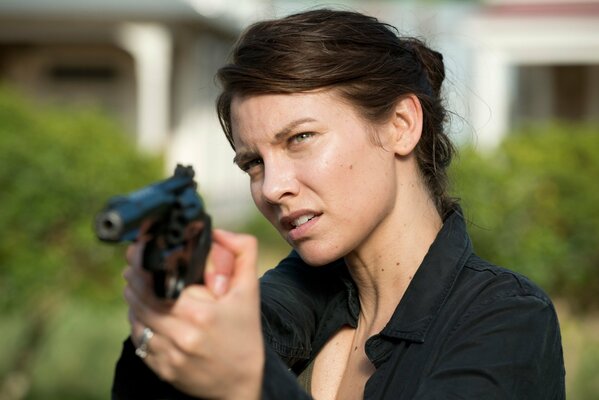 A brown-haired woman with her hair gathered at the back of her head in a black shirt aims a revolver