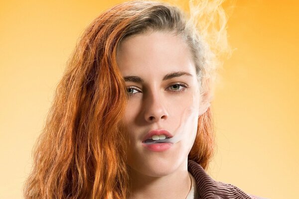 Kristen Stewart aux cheveux roux exhale de la fumée sur fond jaune