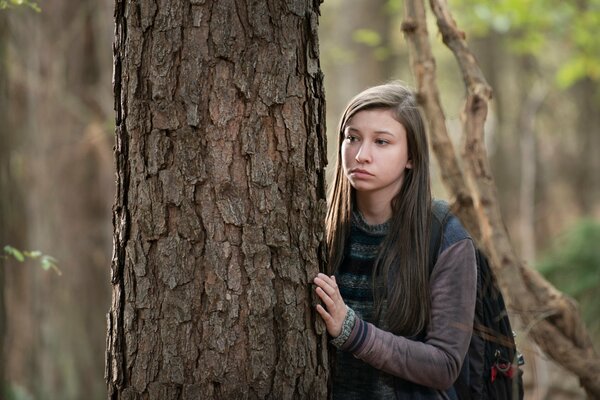 The frightened heroine hides behind a tree in the forest