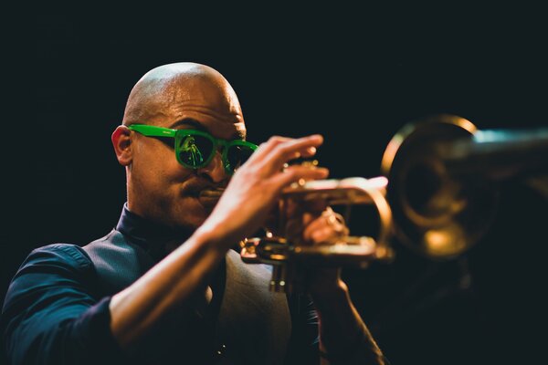 Musicista con gli occhiali verdi che suona la tromba alla luce notturna