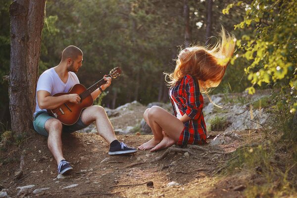 Ein Mann spielt Gitarre neben einem Mädchen im Wald