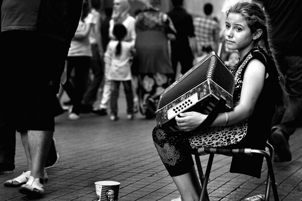 A girl with pigtails plays the accordion for passers-by