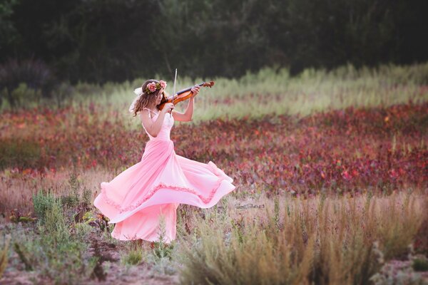 Auf dem Feld wirbelt ein Mädchen in einem rosa Kleid und spielt Geige