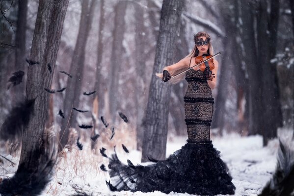 Fille dans le masque et les plumes joue du violon dans la forêt d hiver