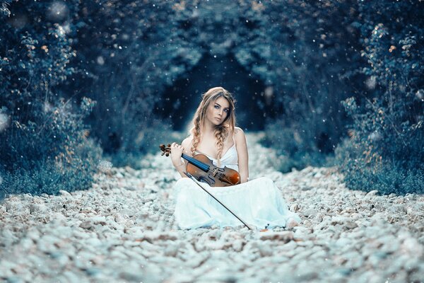 A violinist girl in white sits in the foliage