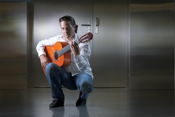 Le guitariste David dans une chemise blanche et un pantalon bleu tient une guitare