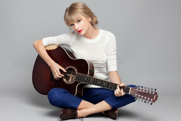 Süße Blondine spielt Gitarre, während sie auf dem Boden sitzt