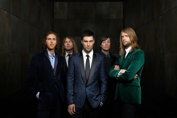 The maroon 5 group in suits stand on a dark background