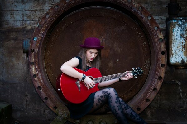 Fille jouant de la guitare rouge, assis dans une roue rouillée