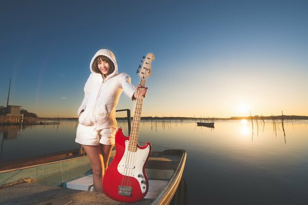 A girl with a red guitar on a sunset background