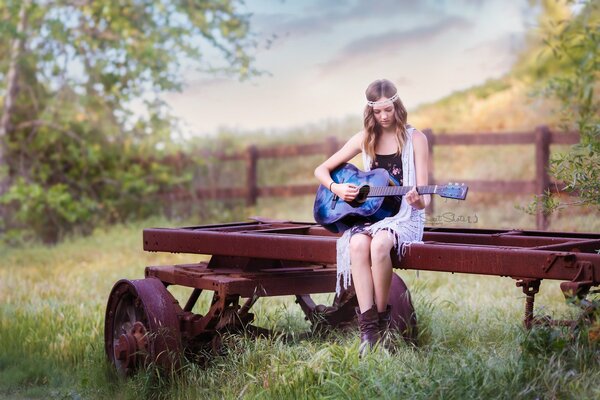 Vor dem Hintergrund der Natur spielt das Mädchen Gitarre, während es auf einem Wagen sitzt