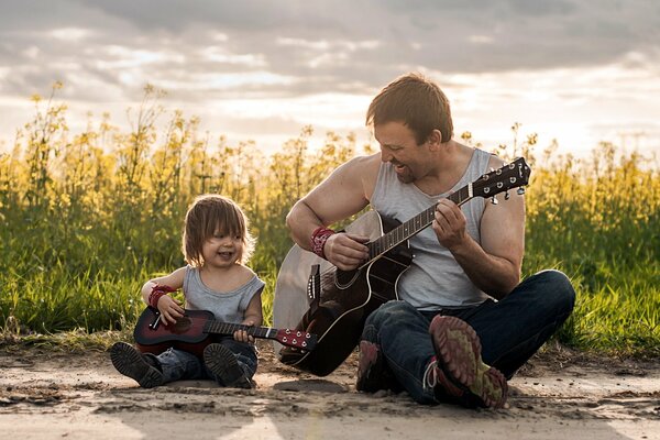 Ojciec i syn grają na gitarach, siedząc na łące