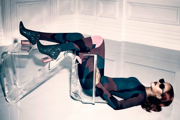 A girl poses lying on the floor with a fallen transparent chair