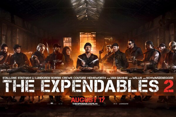 Das Team der Expendables sitzt an einem Tisch, ein Filmplakat