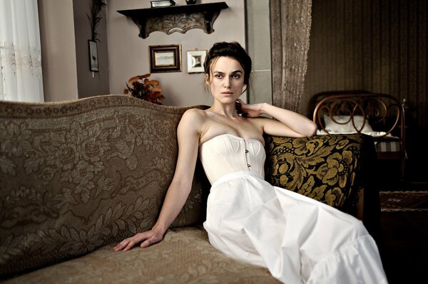 Keira Knightley im weißen Kleid steht auf der couch