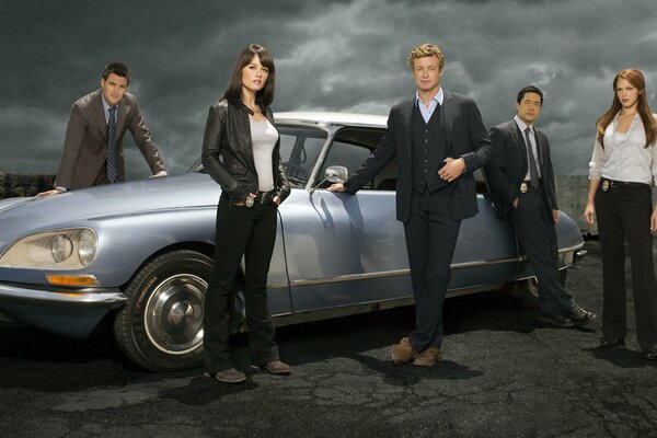 Mentalist actors in black are standing by the car