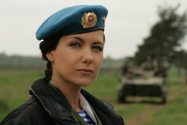 Красивая женщина в военной форме смотрим на зрителя на фоне уезжающего танка