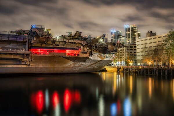 Aircraft carrier with red lights near the city