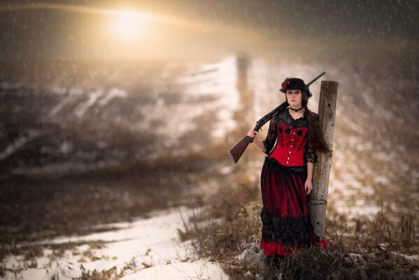 Femme avec un fusil à la main debout parmi la neige et l herbe
