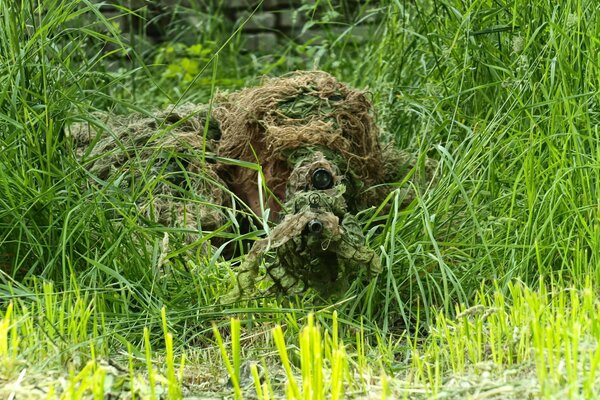 Francotirador disfrazado con rifle, apuntando desde la hierba