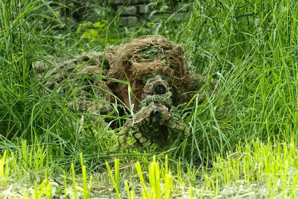 Замаскированный снайпер с винтовкой, прицеливается из травы