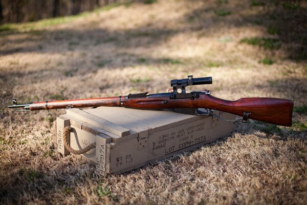 A sniper rifle is lying on a box in the field