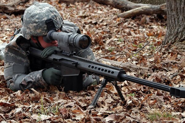 A sniper in the leaves with a rifle in his hands