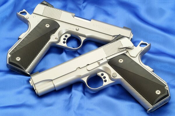 Dos pistolas de plata sobre seda azul