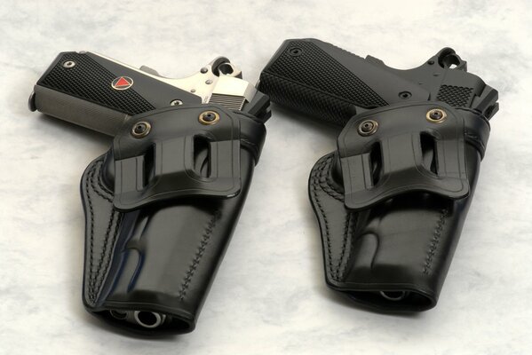 Two pistols in holsters lying on a light surface