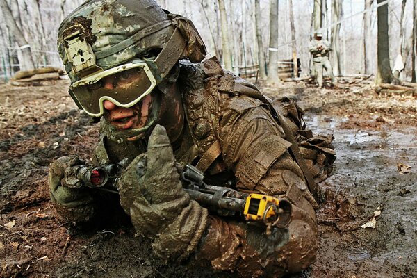 Ein Soldat mit Waffen und Uniform wird ausgebildet, kriecht nach dem Regen auf schmutzigem Boden herum