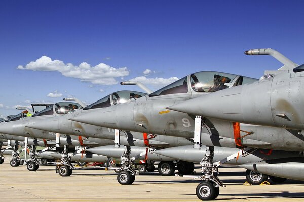 Many military aircraft on the ground are lined up in a row