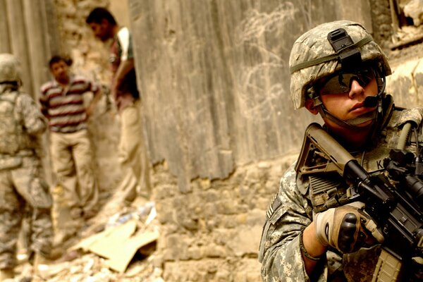 A soldier in Iraq stands with a gun in his hands. Against the background of the people of Iraq