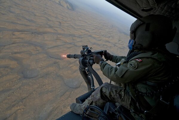 A soldier in a helicopter shoots a machine gun