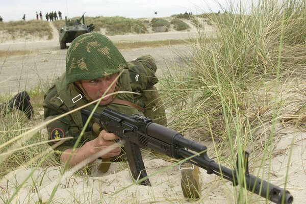 En el campo en los arbustos yace un hombre con un arma