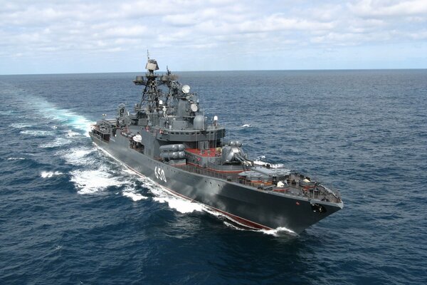 A warship cuts through the waves on the blue sea surface