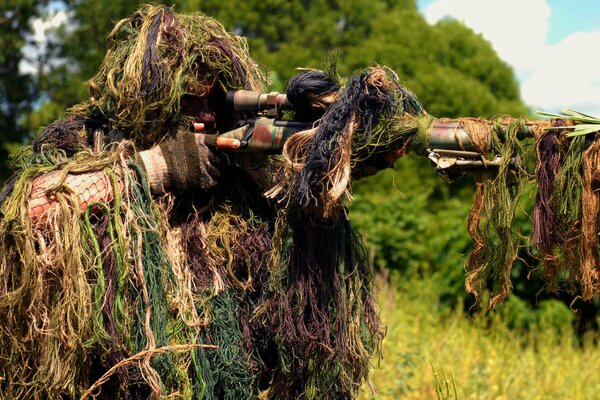 Francotirador en camuflaje bajo la hierba con una ametralladora