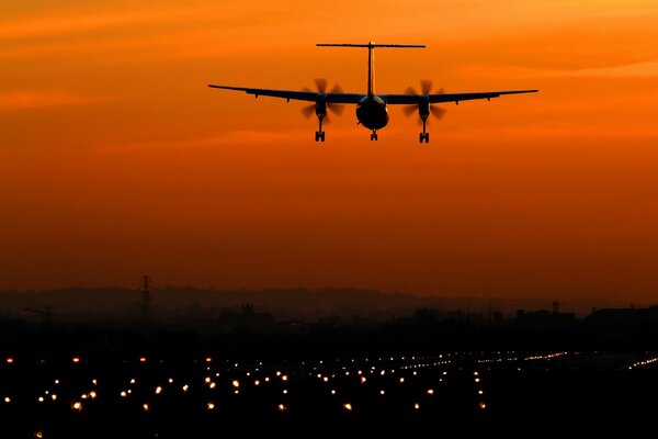 Flugzeug auf Hintergrund des gelben untergehenden Himmels, Lichter der Nachtstadt