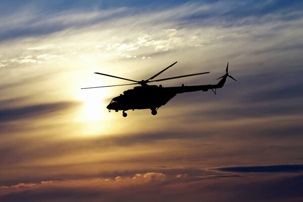 The helicopter flies against the background of the setting sun